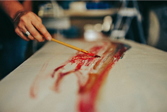 Artist hand applying red paint to canvas with a brush, capturing the creative process in a fine art studio.