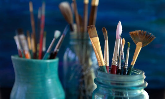 Paintbrushes of various sizes stored in glass jars, representing an artist’s studio tools and the creative process.