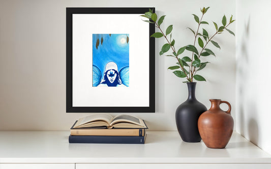 A minimalist styled shelf featuring a framed blue-toned art print of a angel beneath a glowing moon, surrounded by soft gradients and subtle details. The black frame rests above stacked books, with a matte black vase holding leafy branches and a warm-toned ceramic vessel beside it. The clean white surface and natural elements create a calm, balanced, reflective, and contemporary atmosphere.