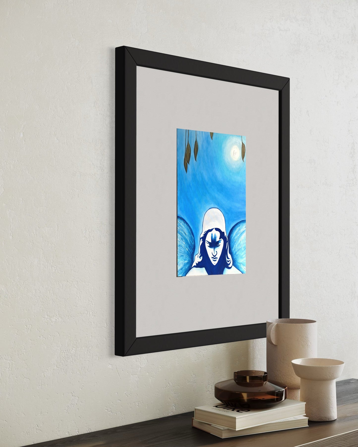 A minimalist styled wooden shelf featuring a framed blue-toned art print of a angel beneath a glowing moon, surrounded by soft gradients and subtle details. The print hung on a white wall, and below on the shelf are stacked books, with two white matte vases and a warm-toned ceramic vessel beside it on two books.  Creating a calm, balanced, reflective, and contemporary atmosphere.