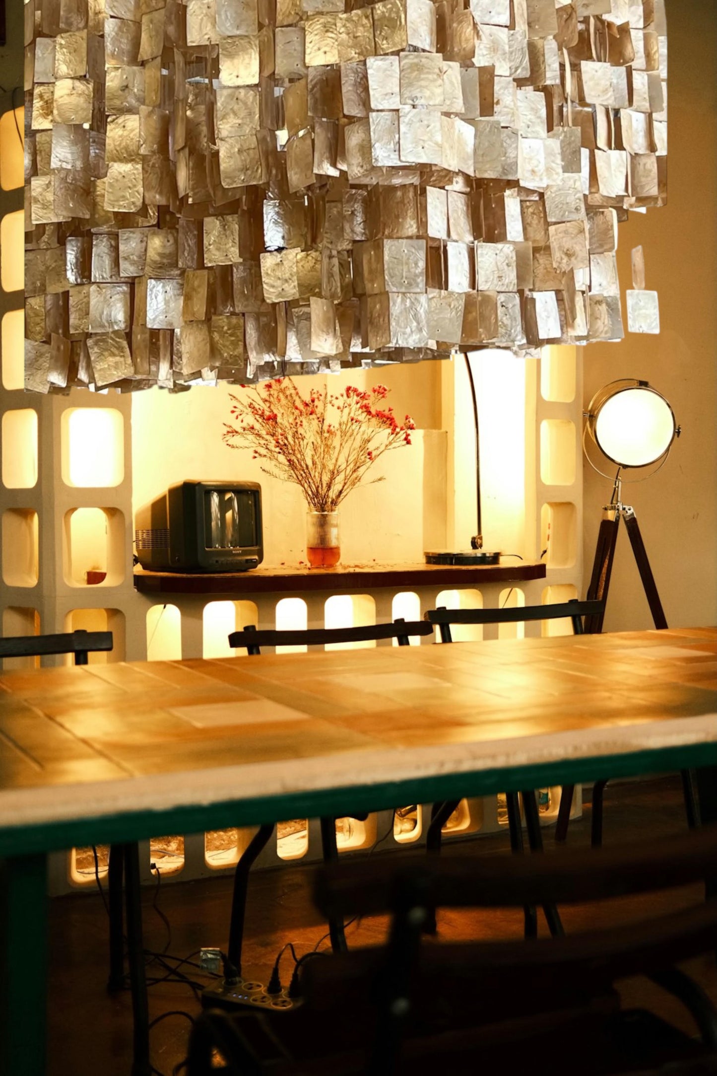 A unique capiz shell chandelier with layered, translucent champaign/golden tiles hangs above a modern dining table, casting a warm, soft glow.  A decorative spotlight decor and build in buffet table that have a golden light.  The textured fixture adds elegance and visual interest, creating a modern yet organic atmosphere.  A focal point for any living room, kitchen, dining area, or foyer.  