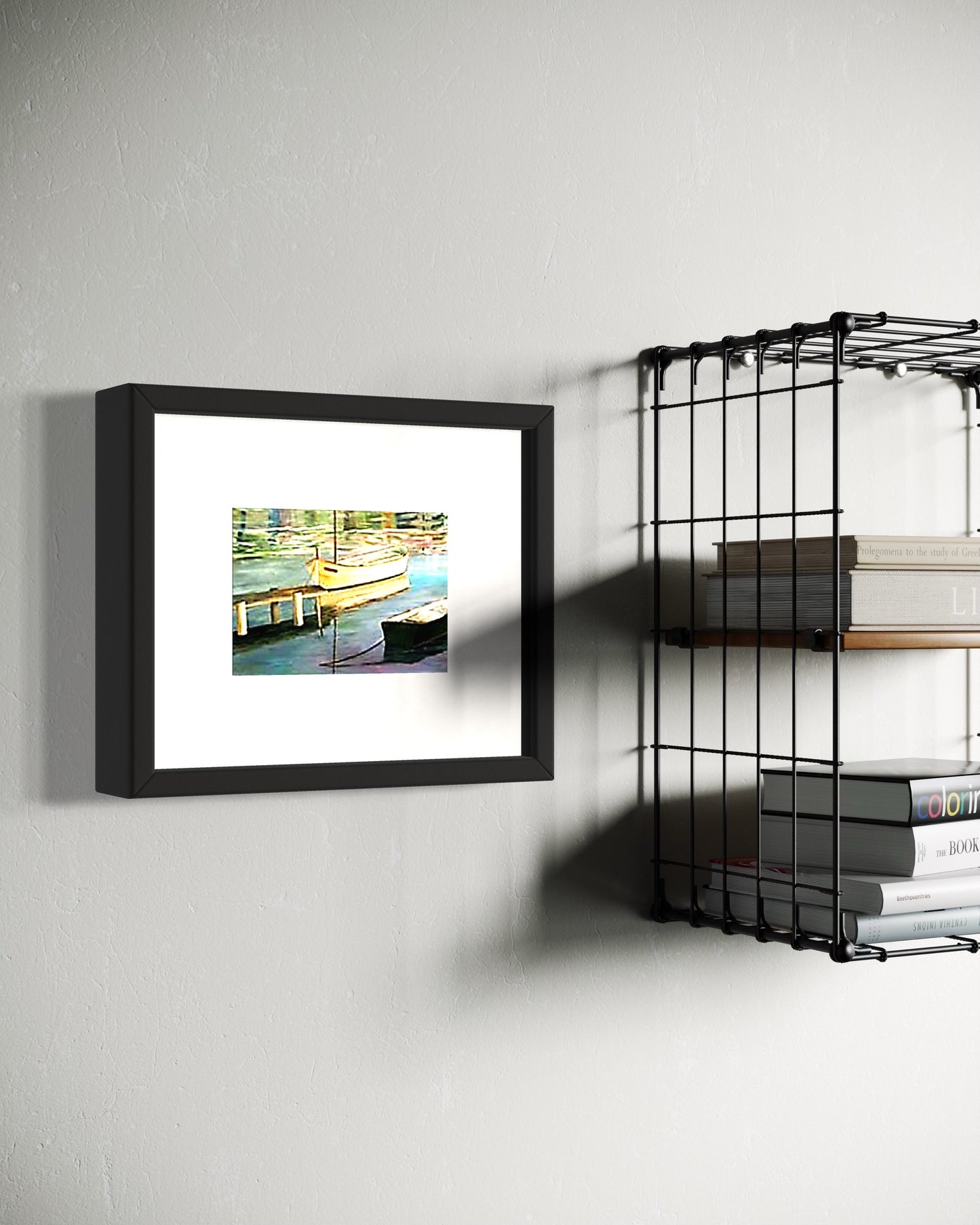 A framed coastal art print of a dock with a small boat reflected in calm water hangs on a white wall.  Next to industrial wire shelves with books.  The scene combines a warm sea side print with industrial shelves, creating a calm, classic atmosphere with a subtle coastal influence.