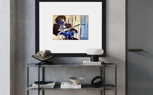 A contemporary interior with a framed print of the blues guitarist, Johnny Lee Hooker, in monochromatic blue and white tones displayed above a grey book shelf and light gray wall. There are books, a ceramic bowl and light on the shelved.  The space feels modern, artistic, and inspired by music and creativity.