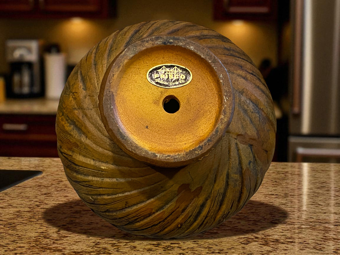 The view from the bottom of a ceramic bowl that shows the makers mark of 'Frisco'.  They all have a textured, woven-style exterior and warm golden glazed interior on a brown marble kitchen counter top. The earthy tones and handcrafted look create a cozy, vintage-inspired feel, suitable for serving food or use as decorative home accents.  Hawaiian decor.    