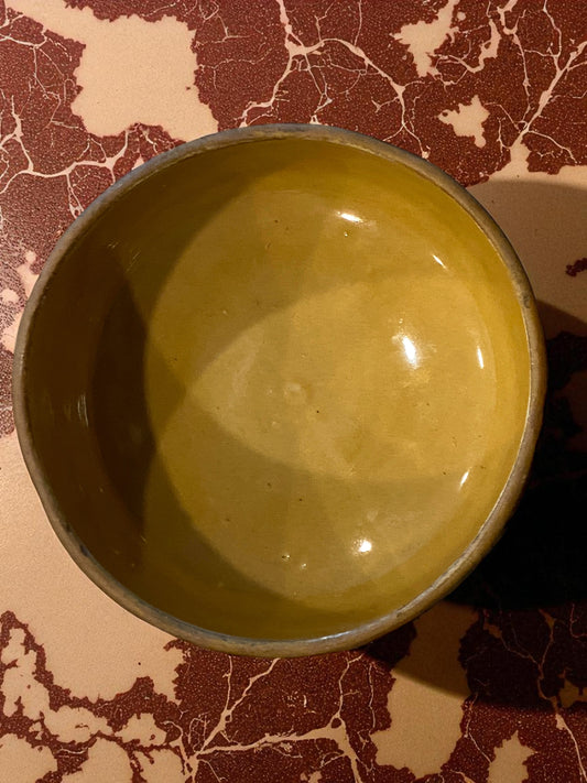 The view from the top of a ceramic bowl with a textured, woven-style exterior and warm golden glazed interior on a brown marble tabletop. The earthy tones and handcrafted look create a cozy, vintage-inspired feel, suitable for serving food or use as decorative home accents.  Hawaiian decor.    