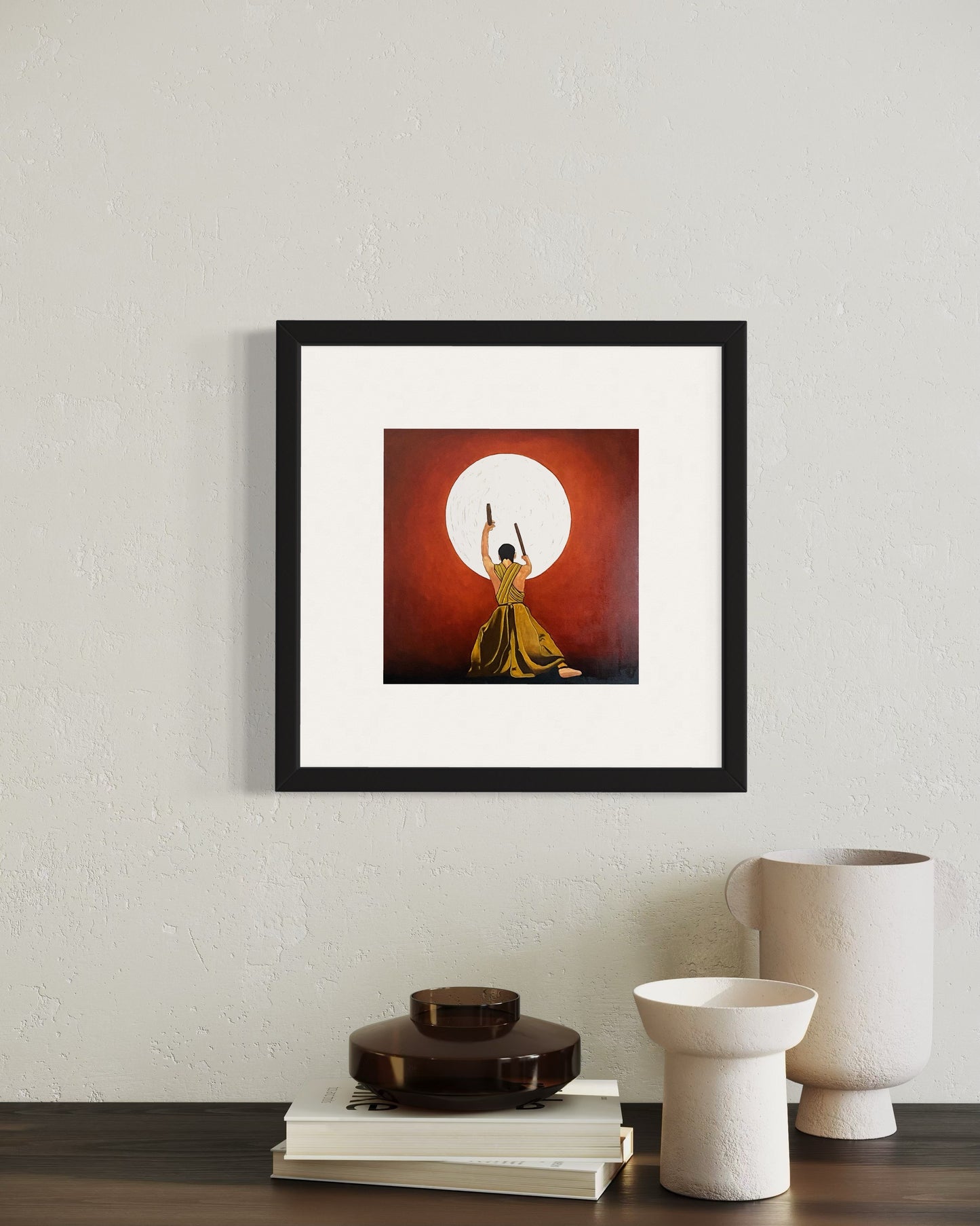 A modern office interior with a framed art print of a silhouetted Japanese Kudo Drummer reaching toward a bright white sun against a red Chinese background on a white wall. Below, a sleek dark wood cabinet holds two modern white vases and some books.  Creating a stylish, vibrant, and inspiring atmosphere.
